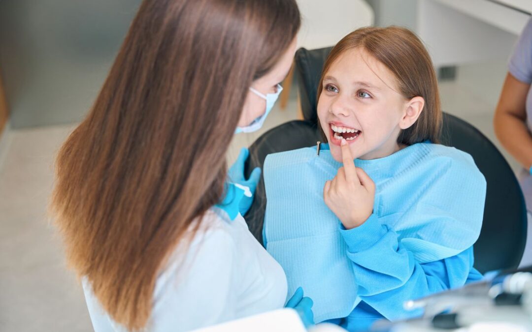 A pediatric dentist examining a child’s teeth while the child points at a dental concern.