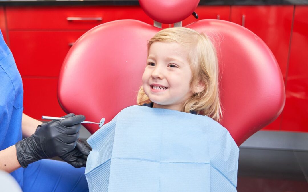 Child smiling during first dental visit while dentist performs gentle oral checkup for early care and comfort.